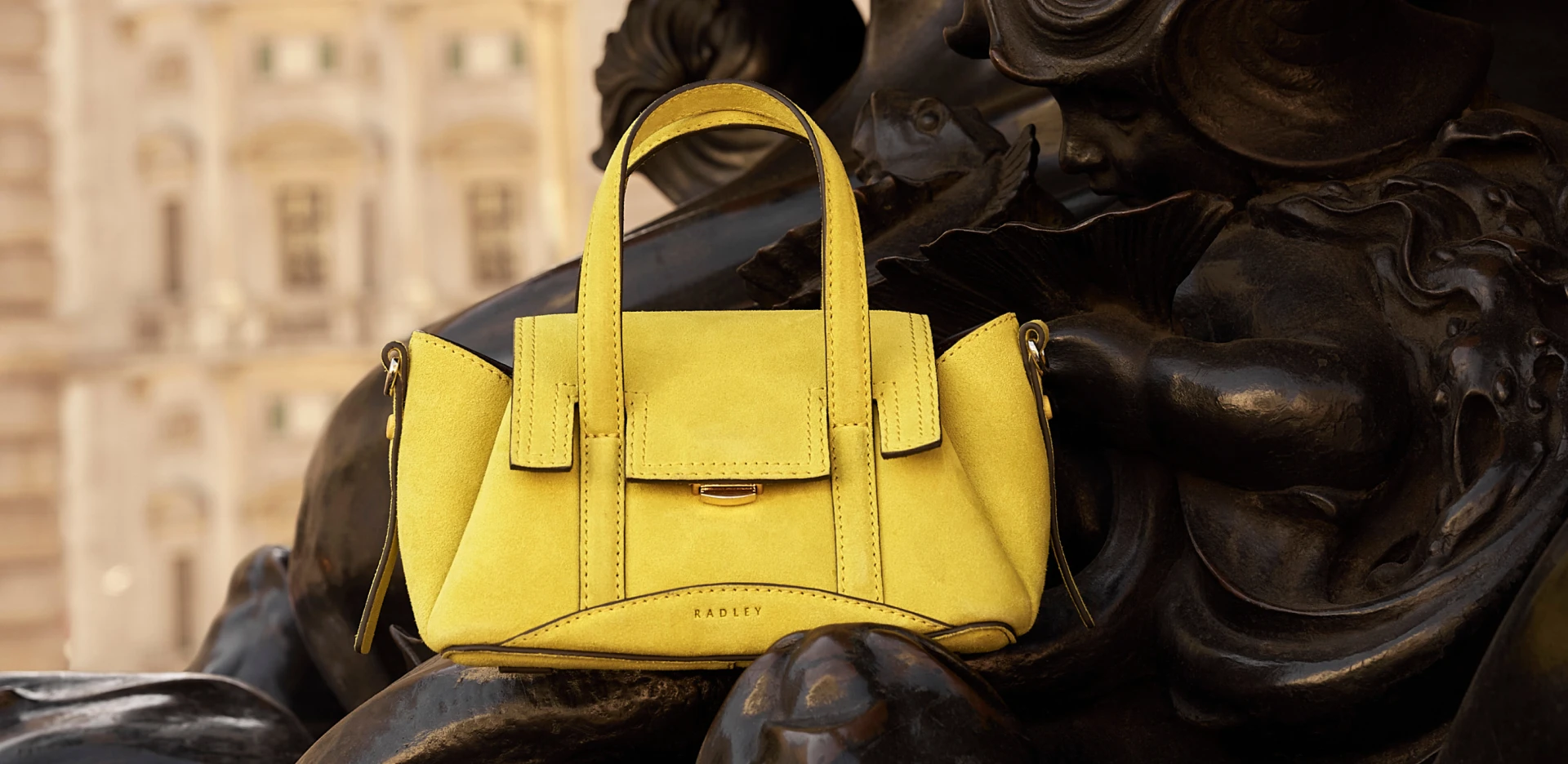 Yellow leather handbag placed on a sculptural statue outdoors, showcasing a fashion accessories product.