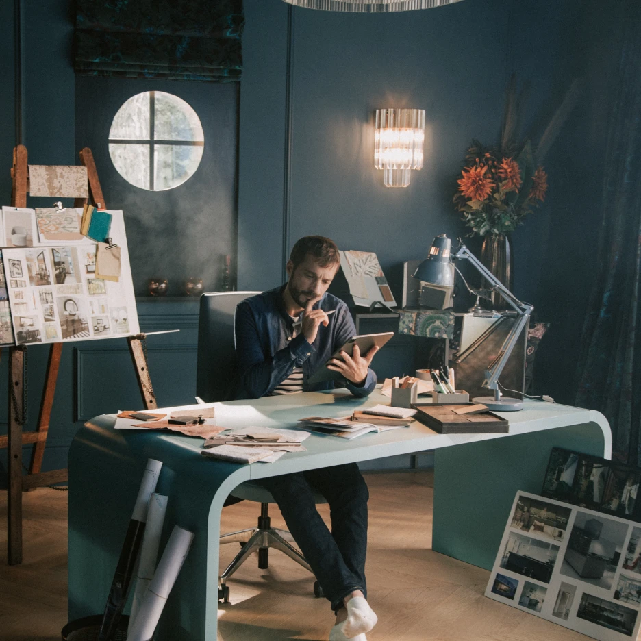 Interior set design workspace with designer at desk reviewing ideas, mood boards and materials in a styled studio environment