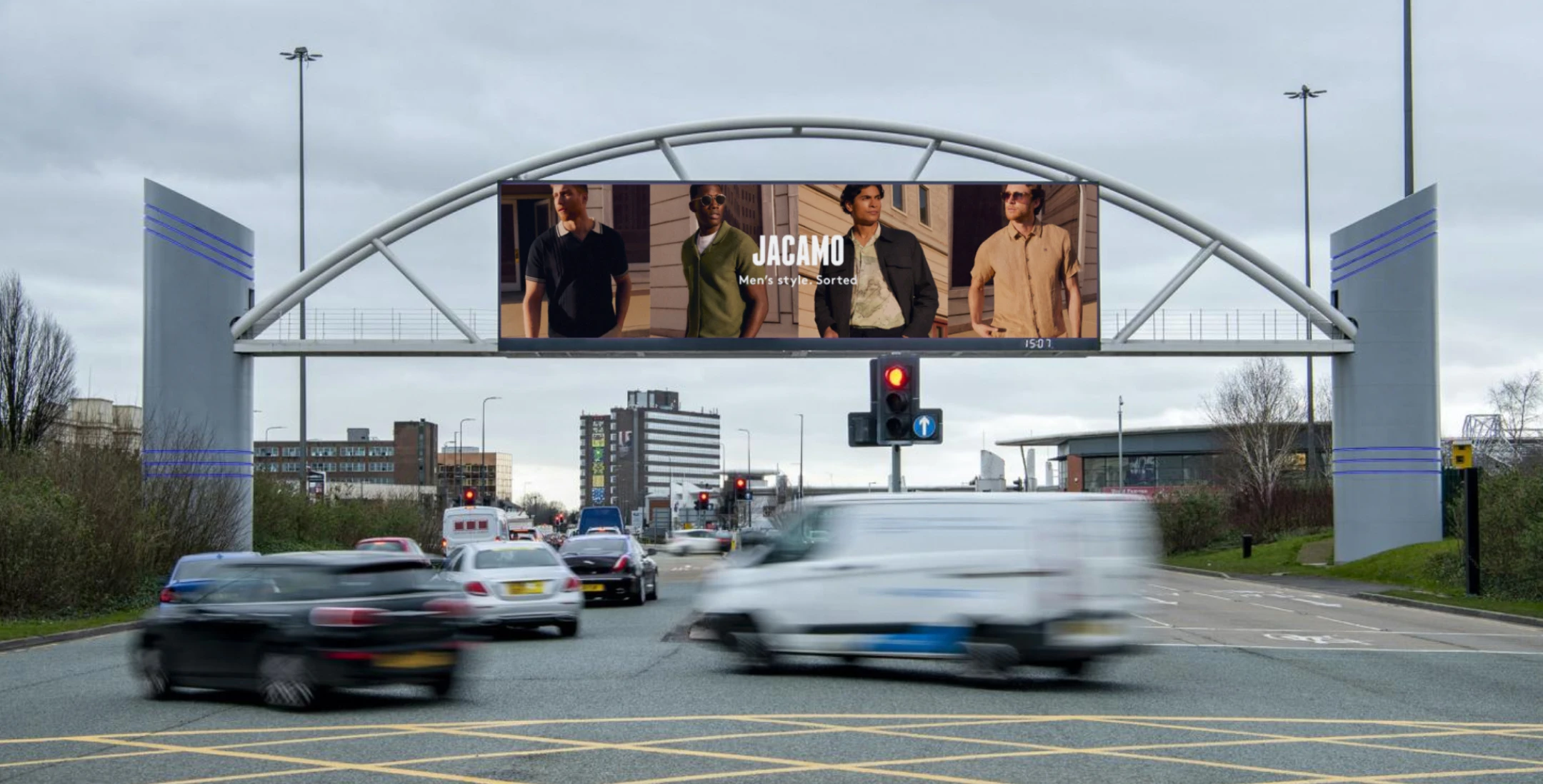Overhead roadside billboard displaying a Jacamo men’s fashion advertisement above a busy urban intersection.