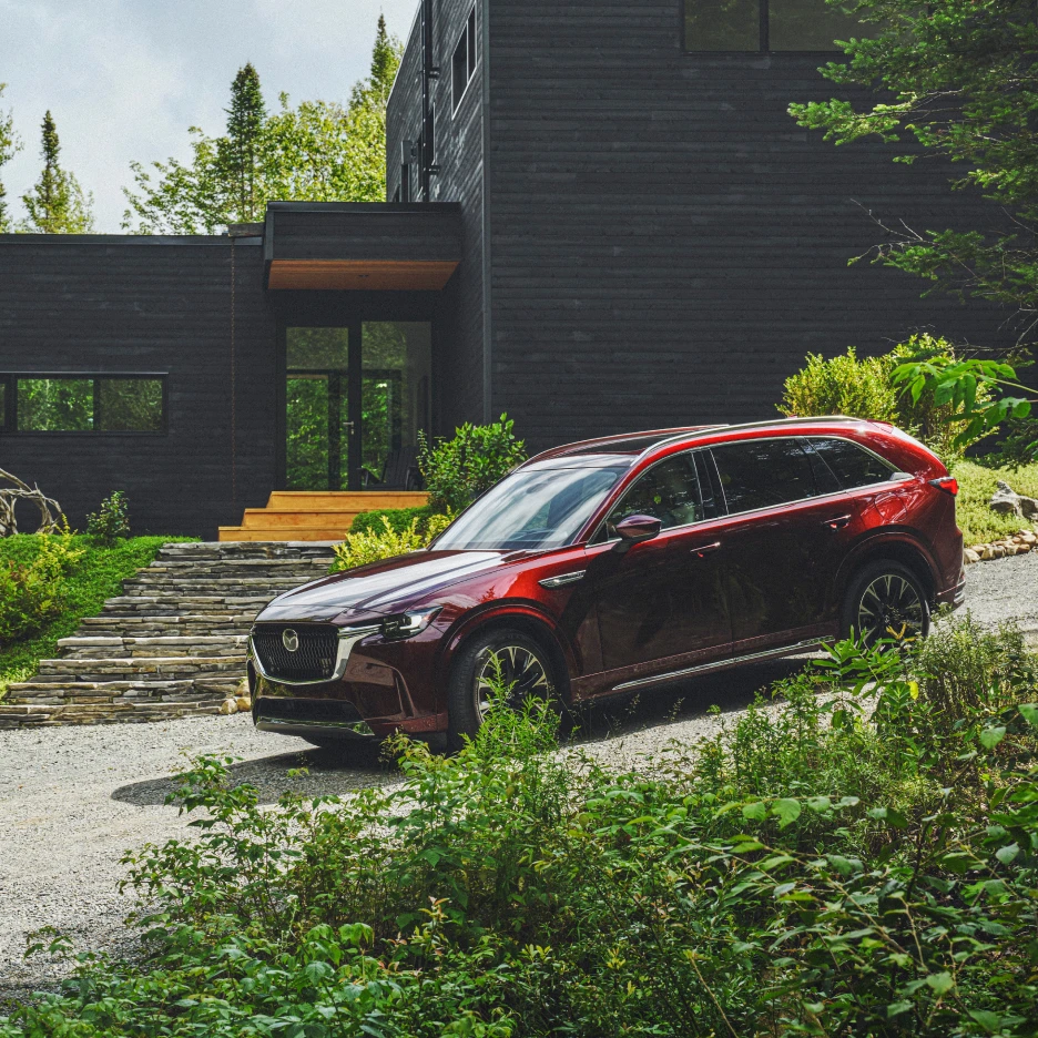 Luxury SUV parked outside a modern black timber house surrounded by greenery, enhanced through professional photo retouching