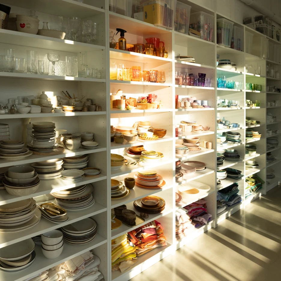Photography studio prop storage shelves filled with plates, glassware, textiles and styling props for shoots
