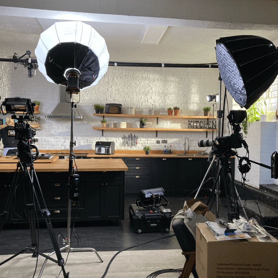Professional livestreaming studio setup with cameras and softbox lighting positioned around a modern kitchen set for filming