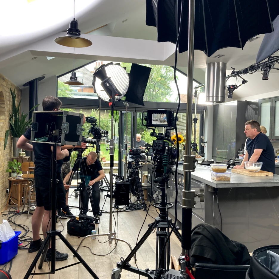 Professional livestream video production setup with cameras, lighting and crew filming a cooking demonstration in a modern kitchen